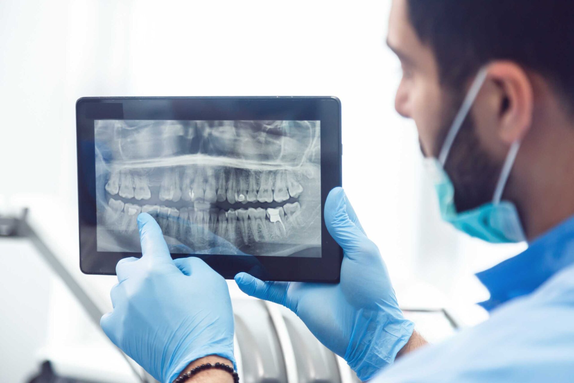 A male dentist examines an X-ray image of patient's teeth