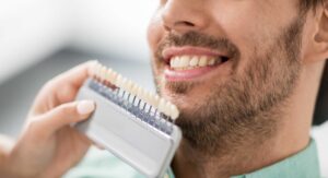 dentist choosing tooth color for patient at clinic, teeth whitening or implants