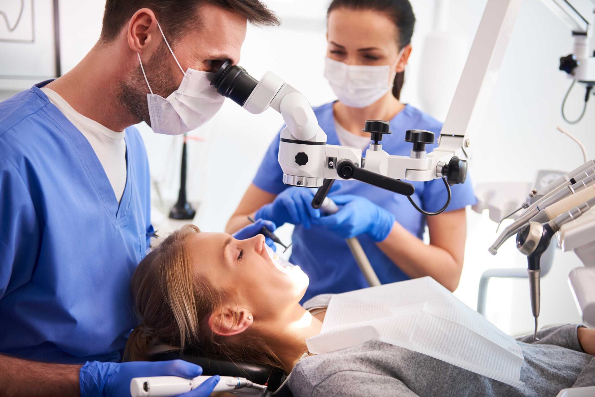 A dentist examines a patient's teeth through a dental microscope