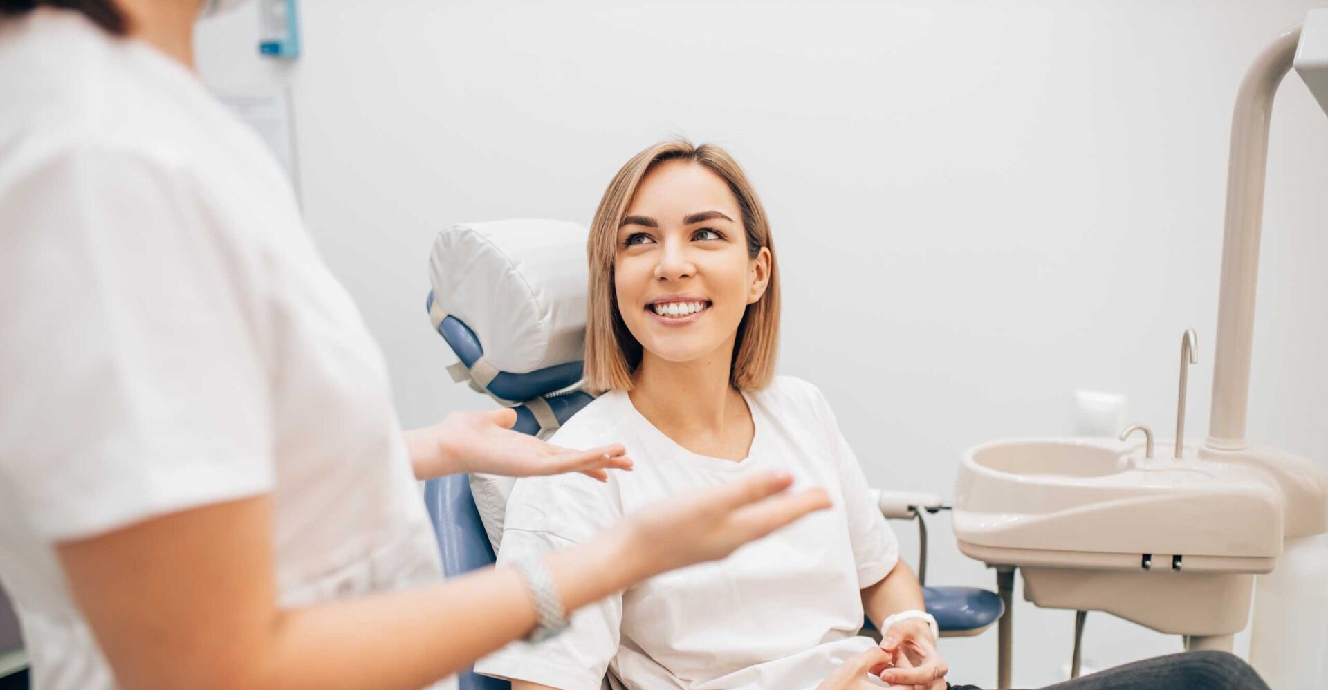 A young woman with short hair smiles up at her dentist as she explains something to her